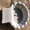 Pila bautismal de mármol con forma de concha.